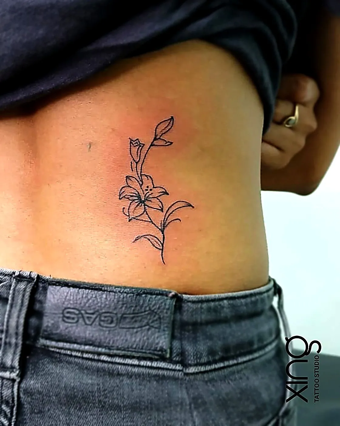 Fine-line lily flower tattoo on ribs
