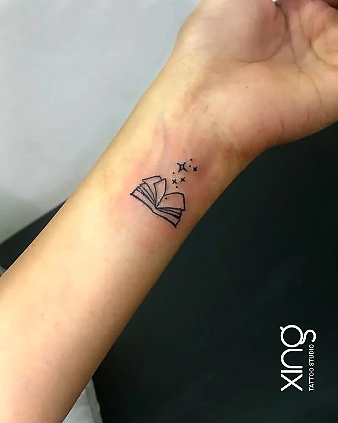 Fine-line open book and stars tattoo on wrist