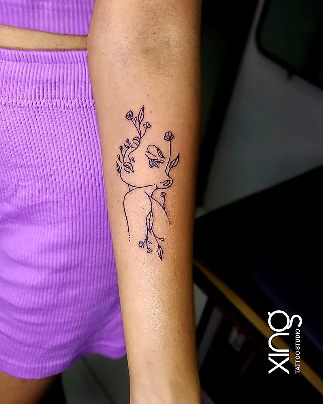 Fine-line floral face line-art tattoo on arm