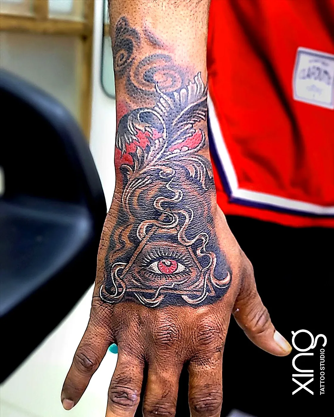 Bold linework all-seeing eye tattoo with red accents on hand