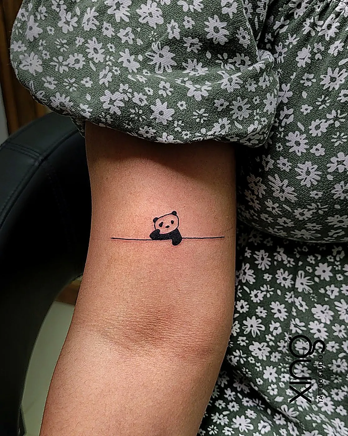 Minimalist line-art panda tattoo on arm