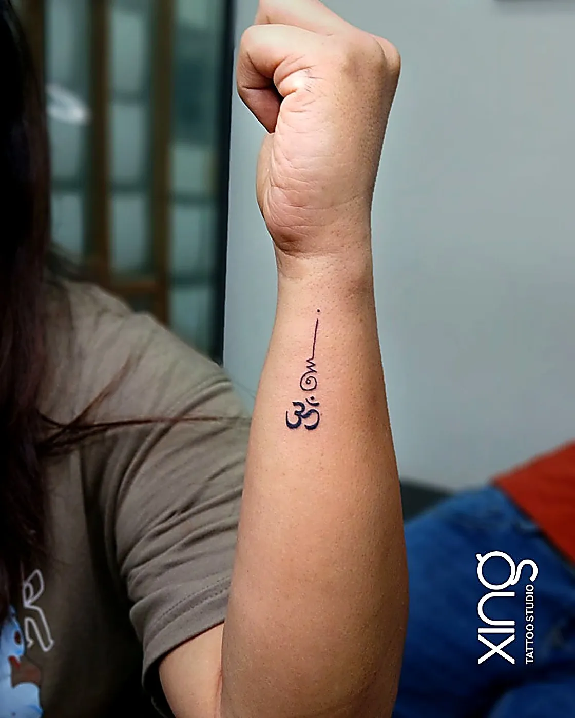 Fine-line Om symbol tattoo on forearm
